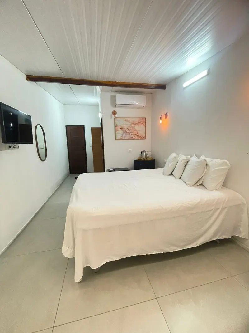 Cama larga com TV de parede, espelho redondo e quadro