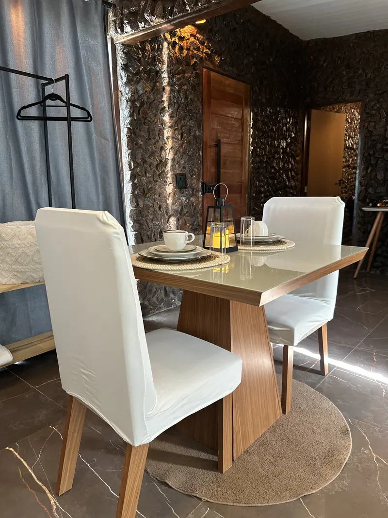 Interior com parede de pedra, mesa para dois e cadeiras estofadas
