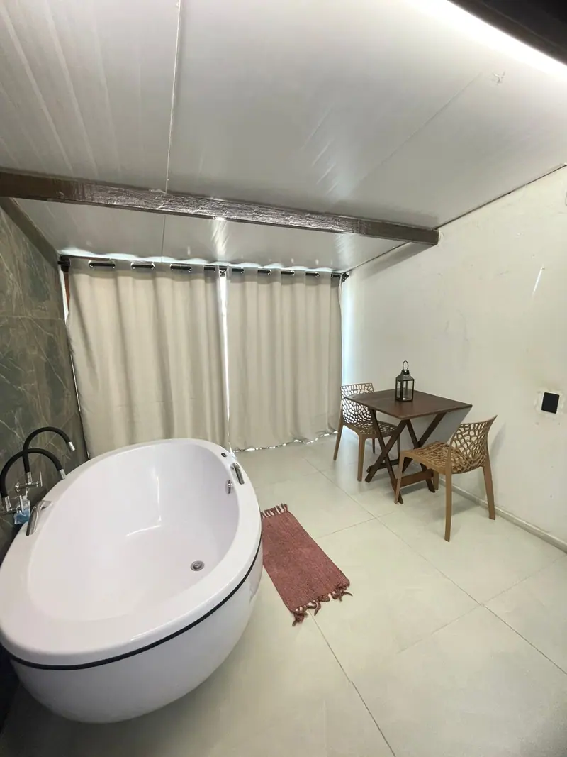 Banheira, revestimento verde, cortinas e mesa com duas cadeiras