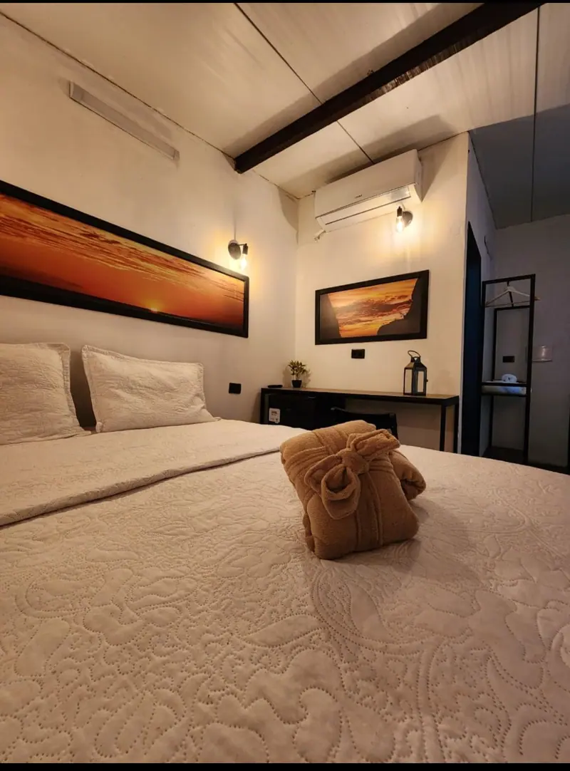 Cama com roupão dobrado, quadro de pôr do sol e escrivaninha